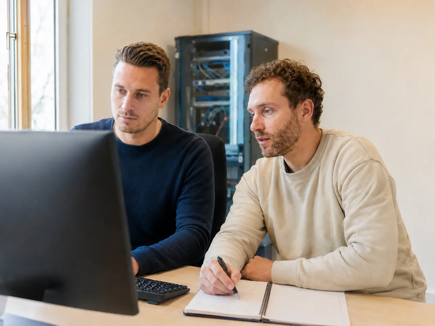 Systeembeheerder en adviseur bekijken samen een beeldscherm terwijl de adviseur aantekeningen maakt.